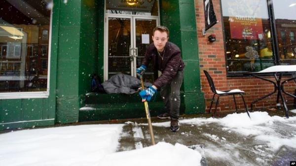 Mikey Reynolds, an employee at The Works on Main Street in Brattleboro, Vt., shovels the sidewalk in front of the restaurant as a person sleeps in the doorway on March 23, 2024. 