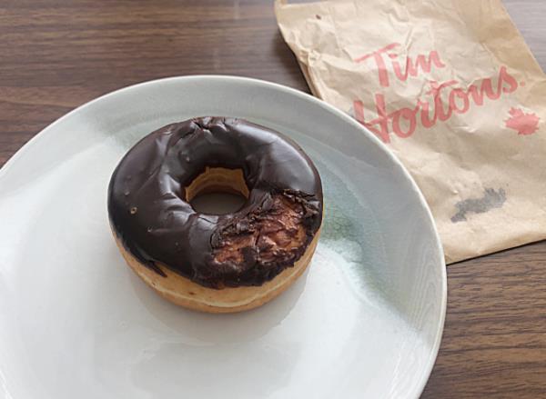 tim horton's chocolate frosted do<em></em>nut on a plate next to a bag 