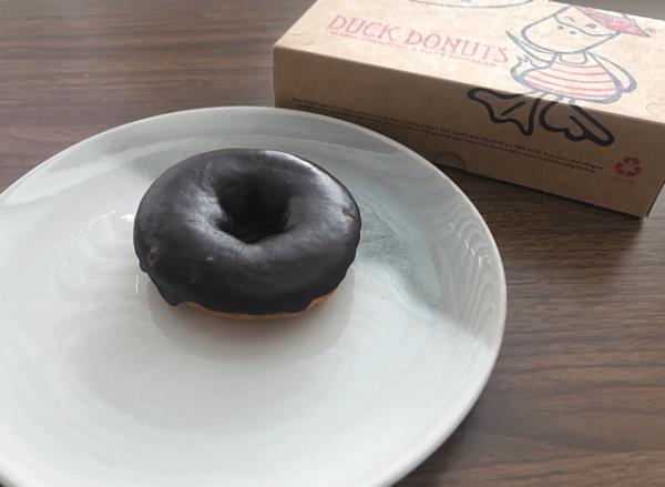a chocolate glazed duck do<em></em>nut on a plate with a do<em></em>nut box 