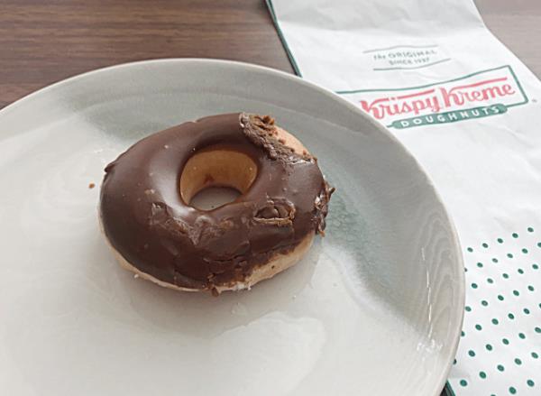 chocolate frosted do<em></em>nut from krispy kreme on a plate next to a bag 