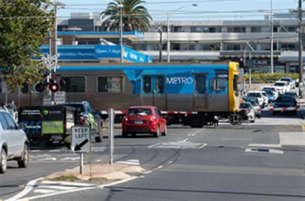 Cars stopped at the level crossing on McDo<em></em>nald Street in Mordialloc as a Metro train passes.