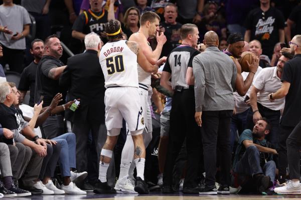 Nikola Jokic reaches for the ball from a fan in the stands.