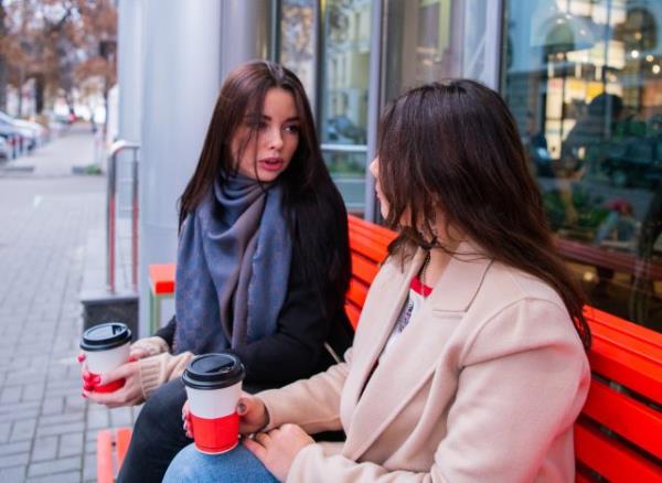friends have serious co<em></em>nvo over coffee on bench outside
