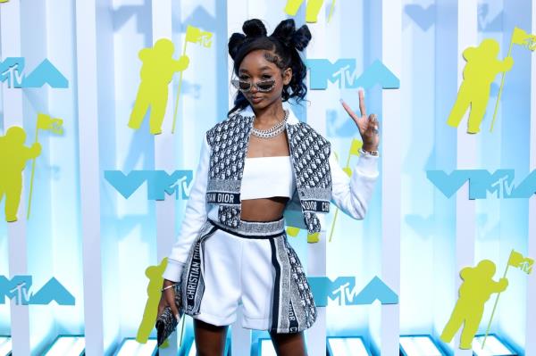 Photo of That Girl Lay Lay. She's making the peace sign and is standing in front of a big MTV banner.