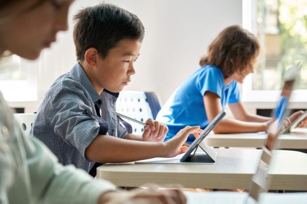 Focused school boy using digital tablet at class in classroom. Attentive junior school student learning o<em></em>nline virtual education digital program app tech during stem computer science lesson.
