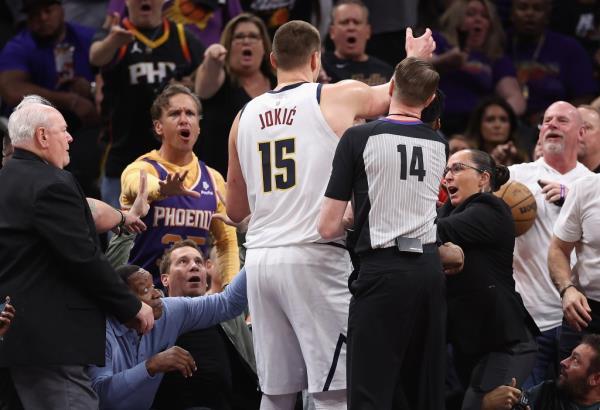 Nikola Jokic #15 of the Denver Nuggets reaches for the basketball after pushing off Phoenix Suns owner Mat Ishbia (L) during the first half of Game Four
