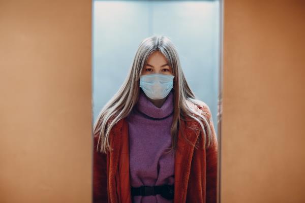 Young chinese woman standing in elevator in medical mask. Doors are closing. Coro<em></em>navirus COVID-19 pandemic concept.