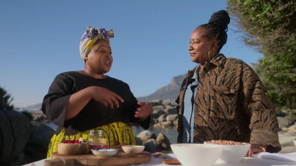 Chef Zola Nena and Chef Alisa Reynolds standing in front of bowls of food outside. 