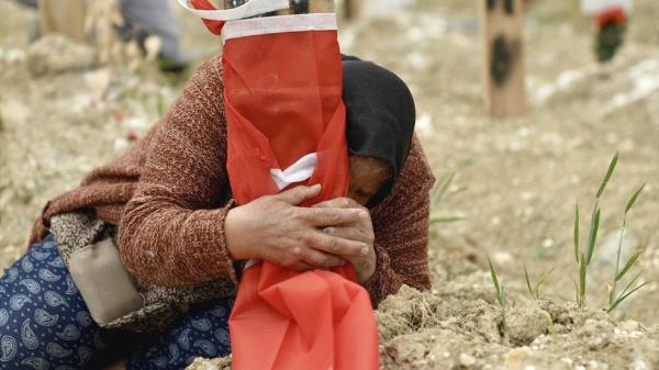 Fethiye Keklik clutching the makeshift grave marker wher<em></em>e her son, who died in the quake, is buried