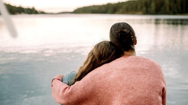 A male parent and a child embrace by a lake