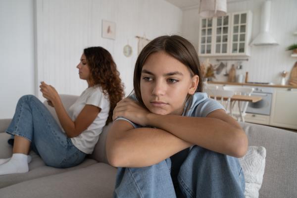 A teen sitting near a parent hunched over her knees.