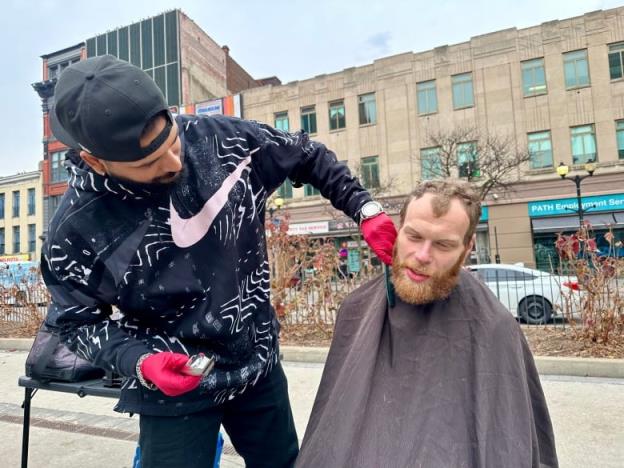 man trims another man's beard outside