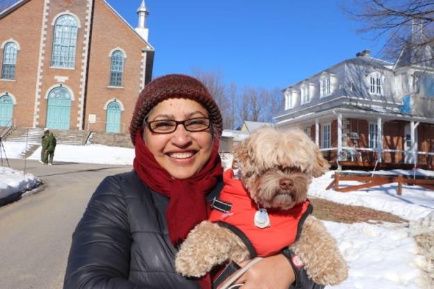 A woman smiles at the camera holding her dog. She is standing in front of a church.
