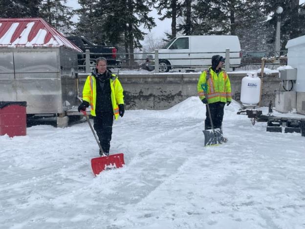 Two men wearing bright neon green jackets hold shovels on the Rideau Canal Skateway
