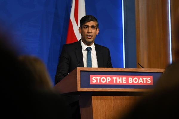 Rishi Sunak speaking at a podium that reads 'stop the boats'