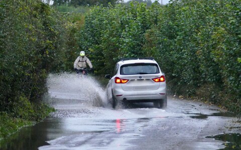A car and cyclist make their way along a water logged country lane in Dunsden, Oxfordshire