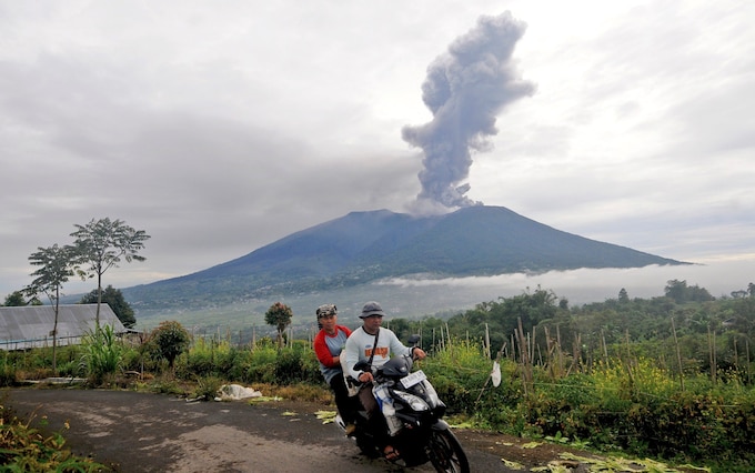 Motorists ride past by as Mount Marapi spews volcanic materials during its eruption in Agam, West Sumatra, Indonesia