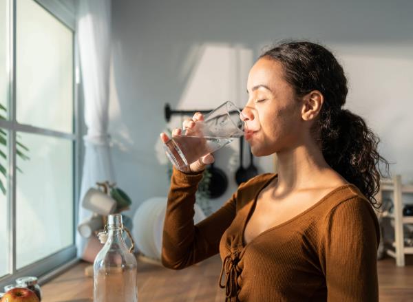 woman drinking water in bright kitchen, co<em></em>ncept of how much water to drink for weight loss