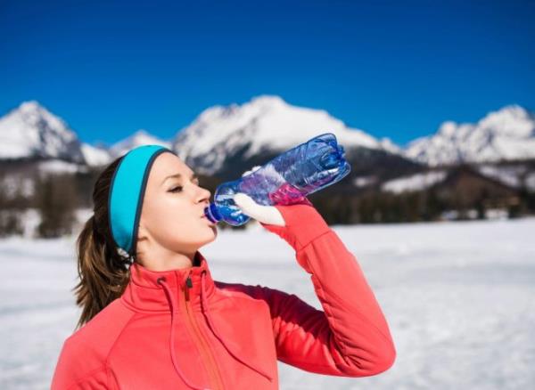 woman drinking water outdoors on snowy day, co<em></em>ncept of reasons to drink more water in winter
