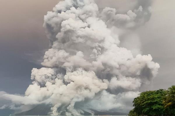 Huge clouds of smoke and ash billowing from the top of the Mount Ruang volcano. The sea is in front, with a boat