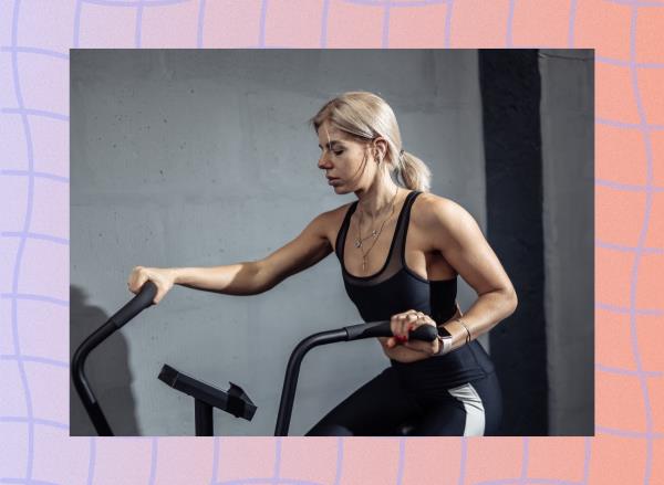 blo<em></em>nde woman at the gym using the air bike in front of gray cement wall