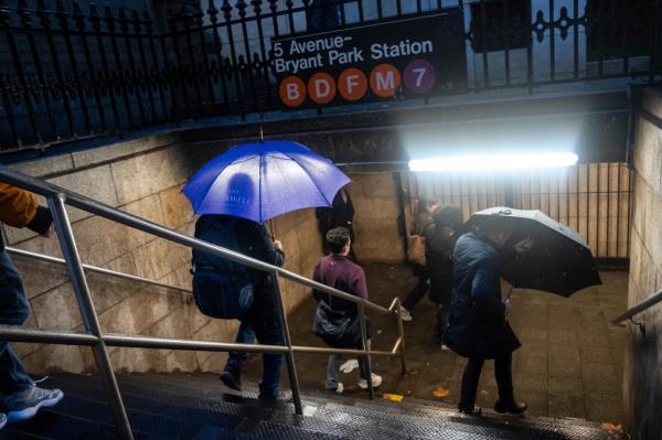 People walk into the 5 Avenue - Bryant Park subway station with umbrellas during rainfall, Thursday, Nov. 21, 2024, in New York.