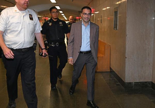 Eric Ulrich, former Commissio<em></em>ner of Buildings, in a brown sports jacket, walking down a hallway in court with police officers