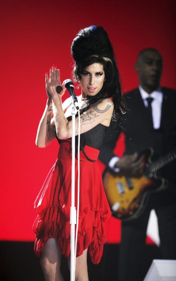 Amy Winehouse performing on stage at The BRIT Awards 2007 in a red dress holding a microphone