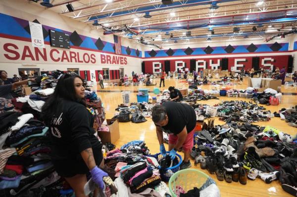 Evacuated locals gather among piles of clothes and shoes in a sports stadium