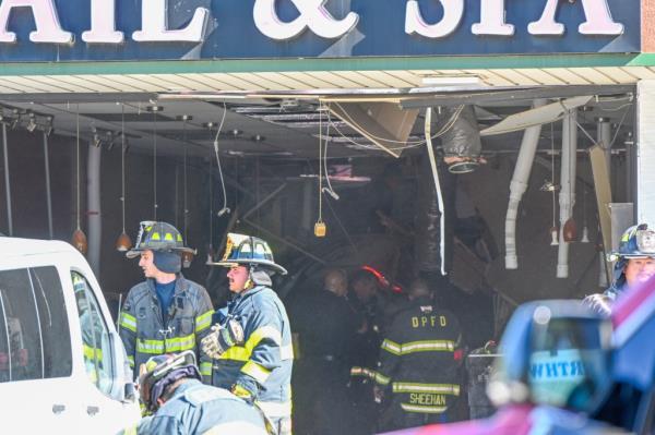 Firefighters examining a damaged nail salon after a vehicle crashed into it, causing fatalities and injuries