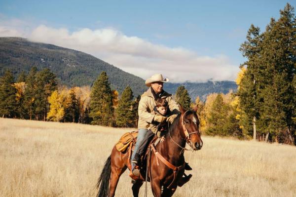 Kevin Costner riding a horse in a field. 