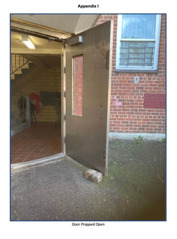 A propped open entry door with a window in a NYCHA residential building, showing issues with building entry door security.