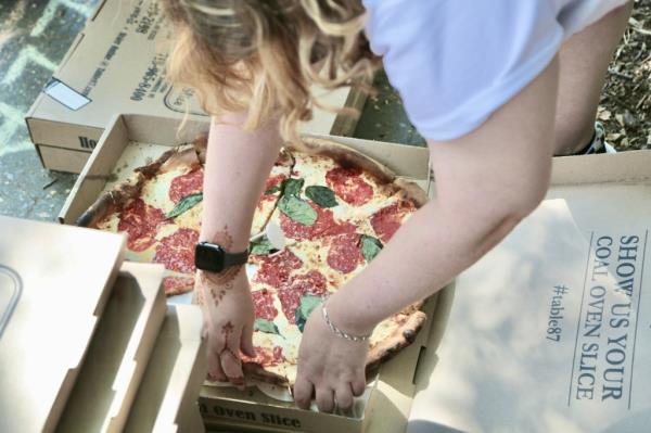 Worker handing out pizza slices from box.