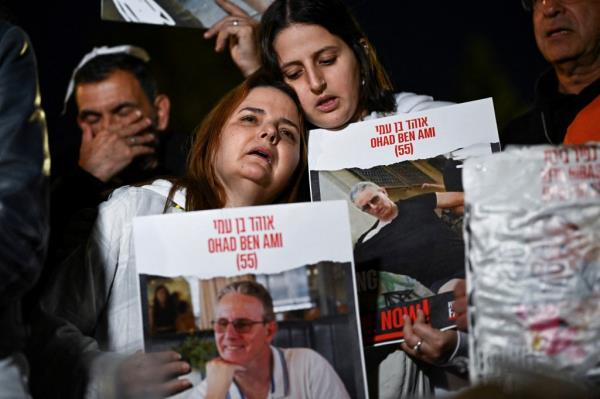 Two Israeli women hold signs with photos of  hostages being held by Hamas during a protest. 