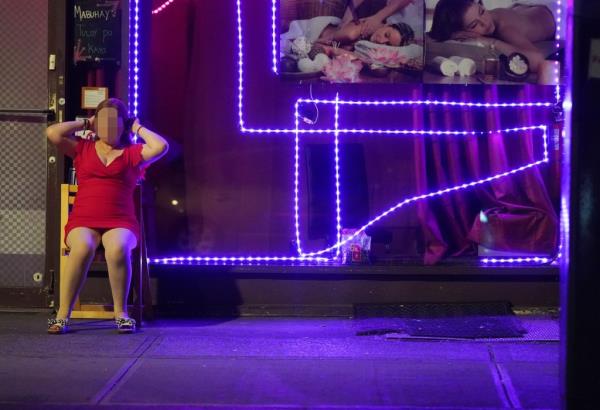 A woman believed to be a sex worker is pictured sitting in front of a storefront.