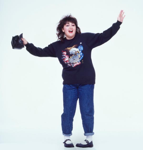 Roseann Barr in jeans in a patriotic sweatshirt in 1986, full length, white background. 