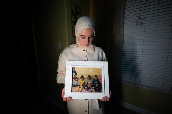 Maryam Kamalmaz hold a photo of her father with some of his 14 grandchildren in Grand Prairie, Texas