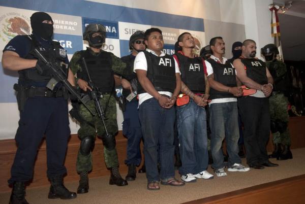 Lineup of alleged Zeta cartel members guarded by officials with large guns and tactical gear.