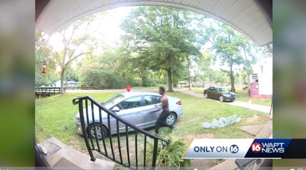 Man and women kneel behind car as gunman aims firearm towards them.