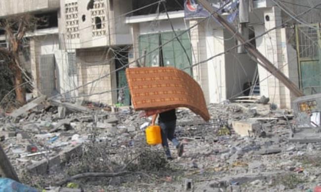 Palestinian citizens evacuate their homes damaged by Israeli airstrikes on October 10, 2023 in Gaza City. A man holding a jerry can and using a mattress as a shield runs among rubble and debris from destroyed buildings