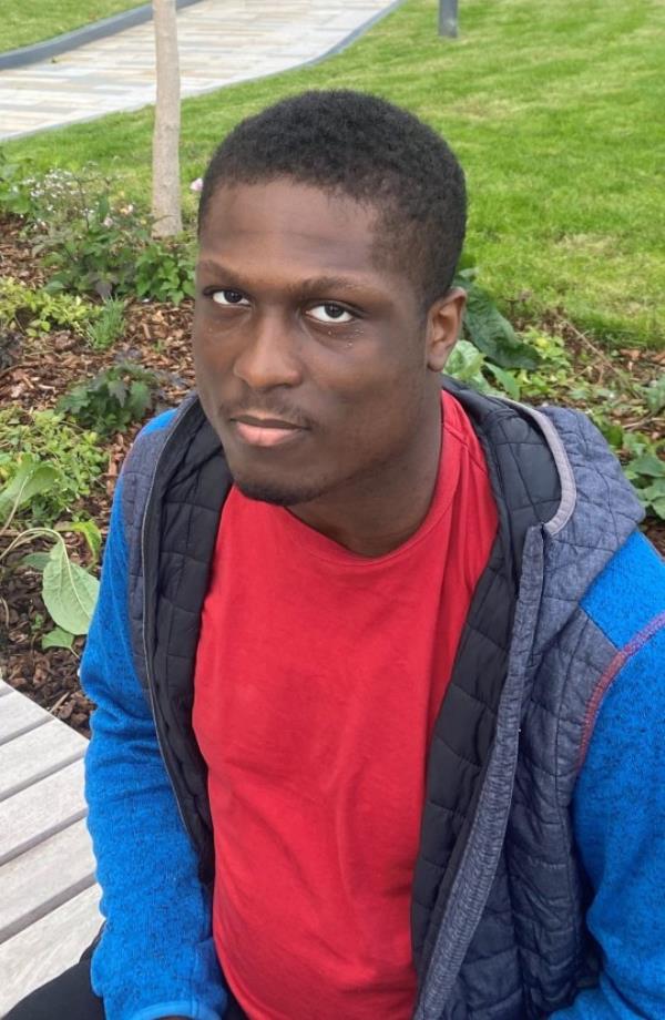 Levi sitting on a bench, looking to camera, wearing a red t-shirt and blue jacket